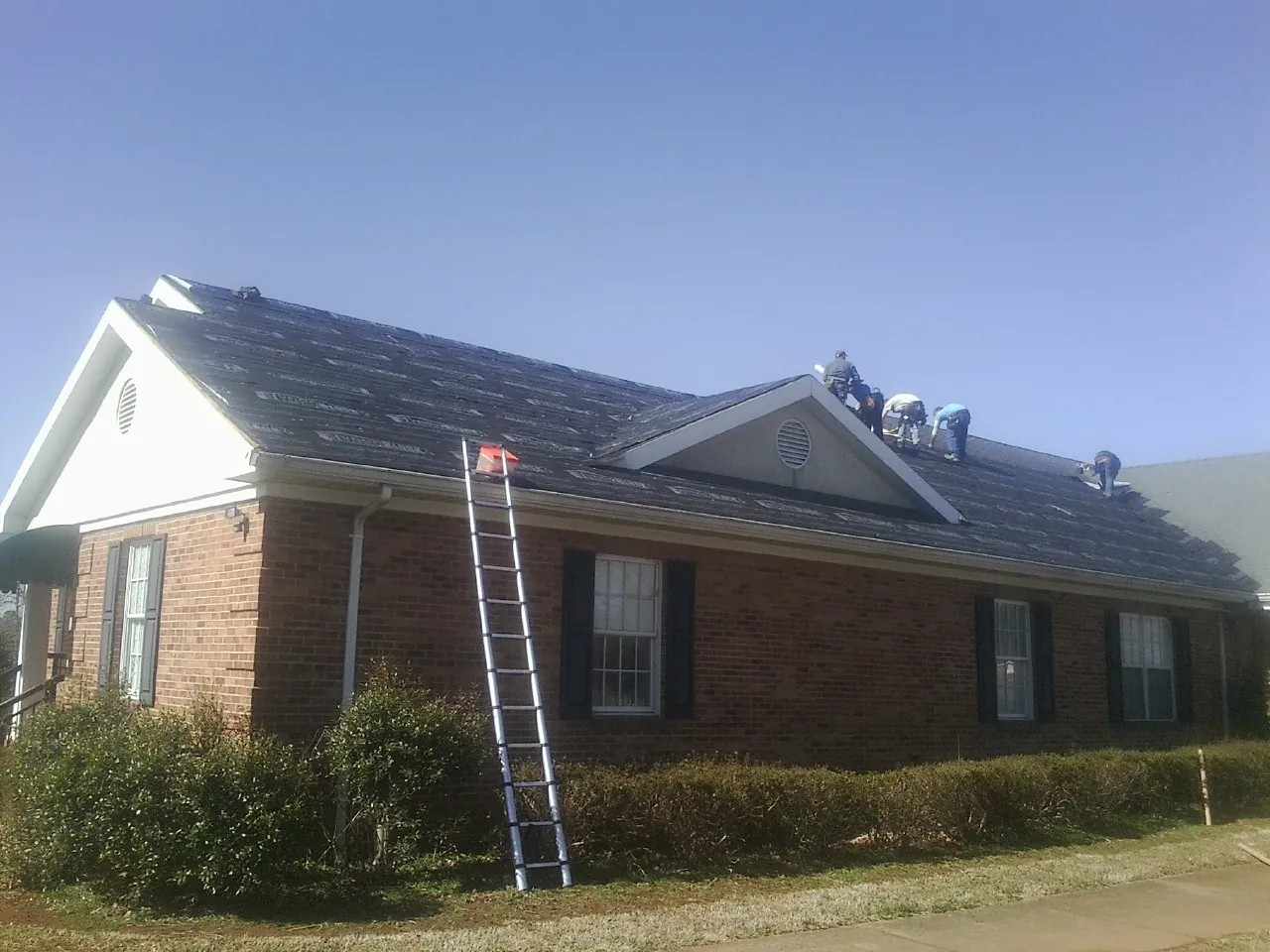Crew tearing shingles off a brick ranch roof with a ladder set — Metal Roof Repair work by our crew in Roxbury