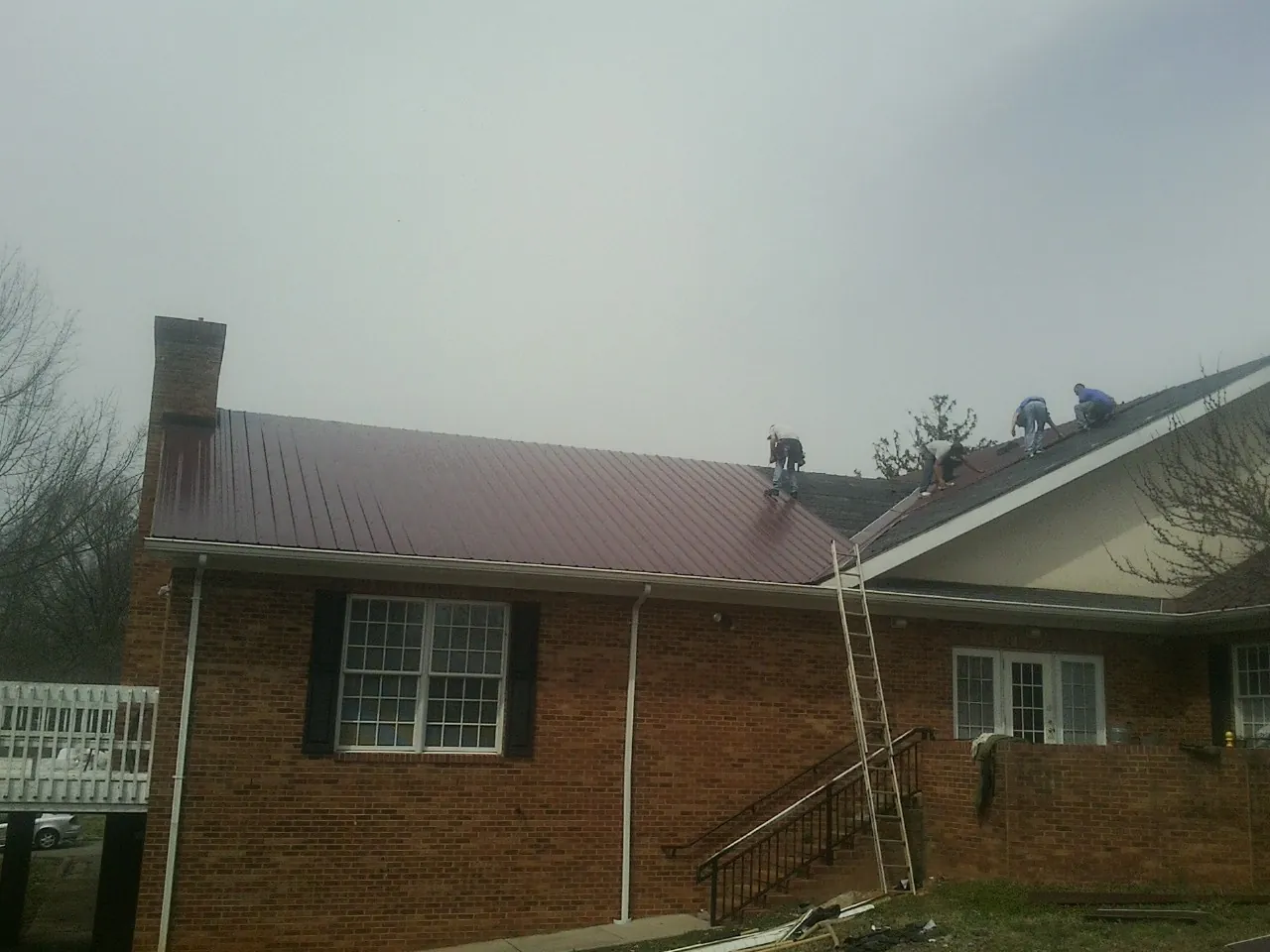Crew setting red metal roofing panels on a brick home in Roxbury