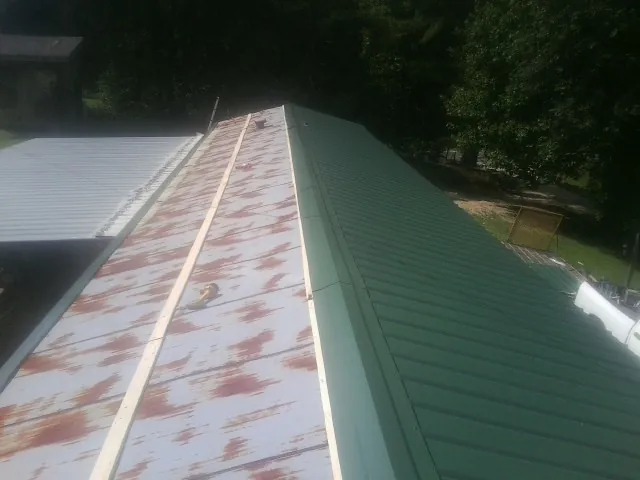 Old rusted panels beside newly installed green metal roofing — Wind Damage Roof Repair by Roofing Brothers in Roxbury