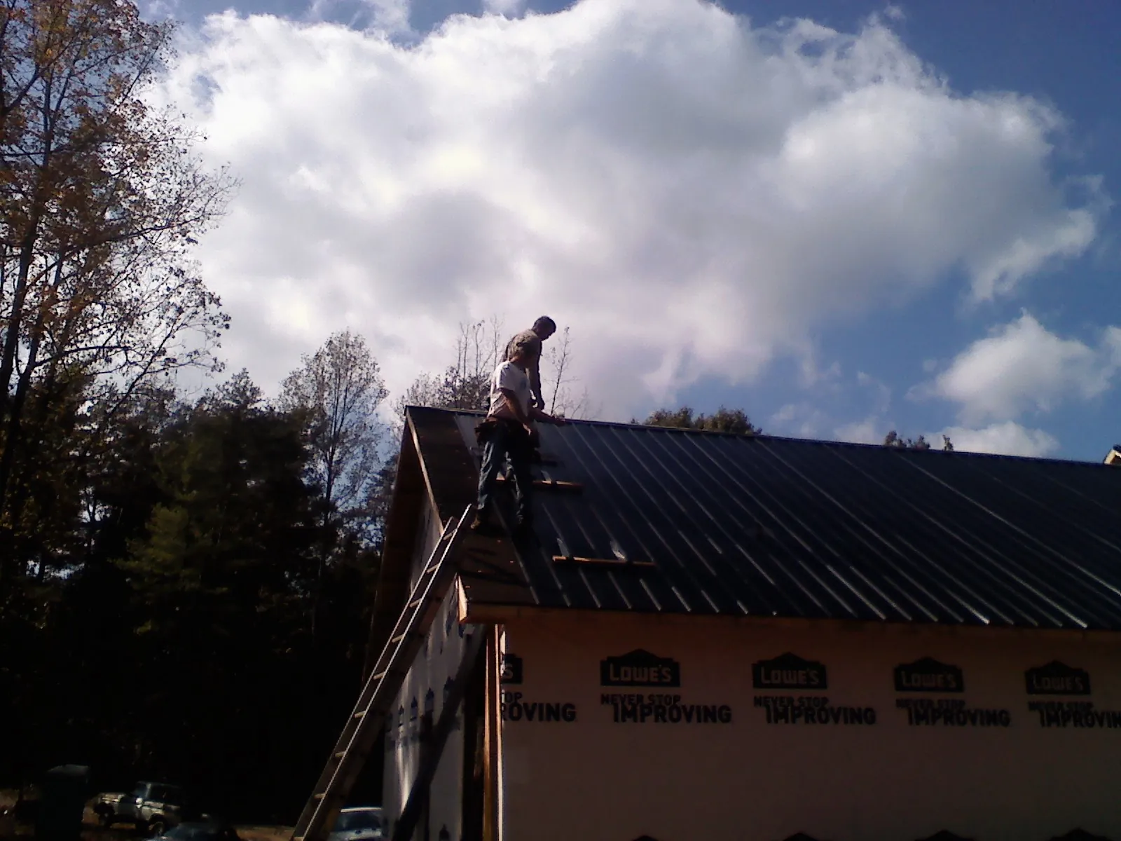 Roofer fastening dark metal panels high against a cloudy sky, from a Roof Inspection job in Roxbury