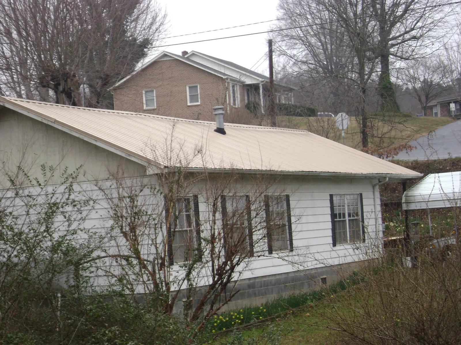 Tan metal roof on a white sided house set into a hillside — Commercial Roofing by Roofing Brothers in Roxbury